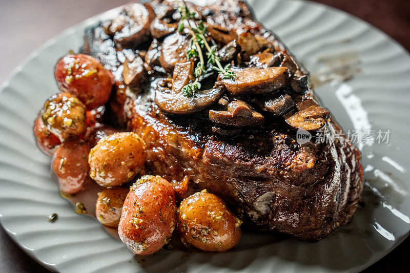 Juicy rib eye steak cooked perfectly, served with sautéed mushrooms and baby potatoes, beautifully presented on a white plate. A delicious and elegant dish